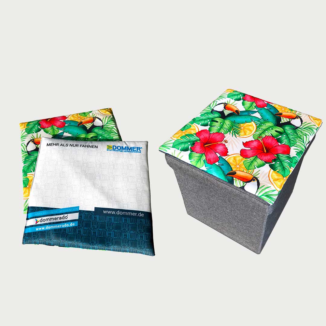 Sitzkissen mit bedruckter Bespannung, neben einem grauen BoxSeat-Hocker mit tropisch gemustertem, farblich passendem Sitzkissen